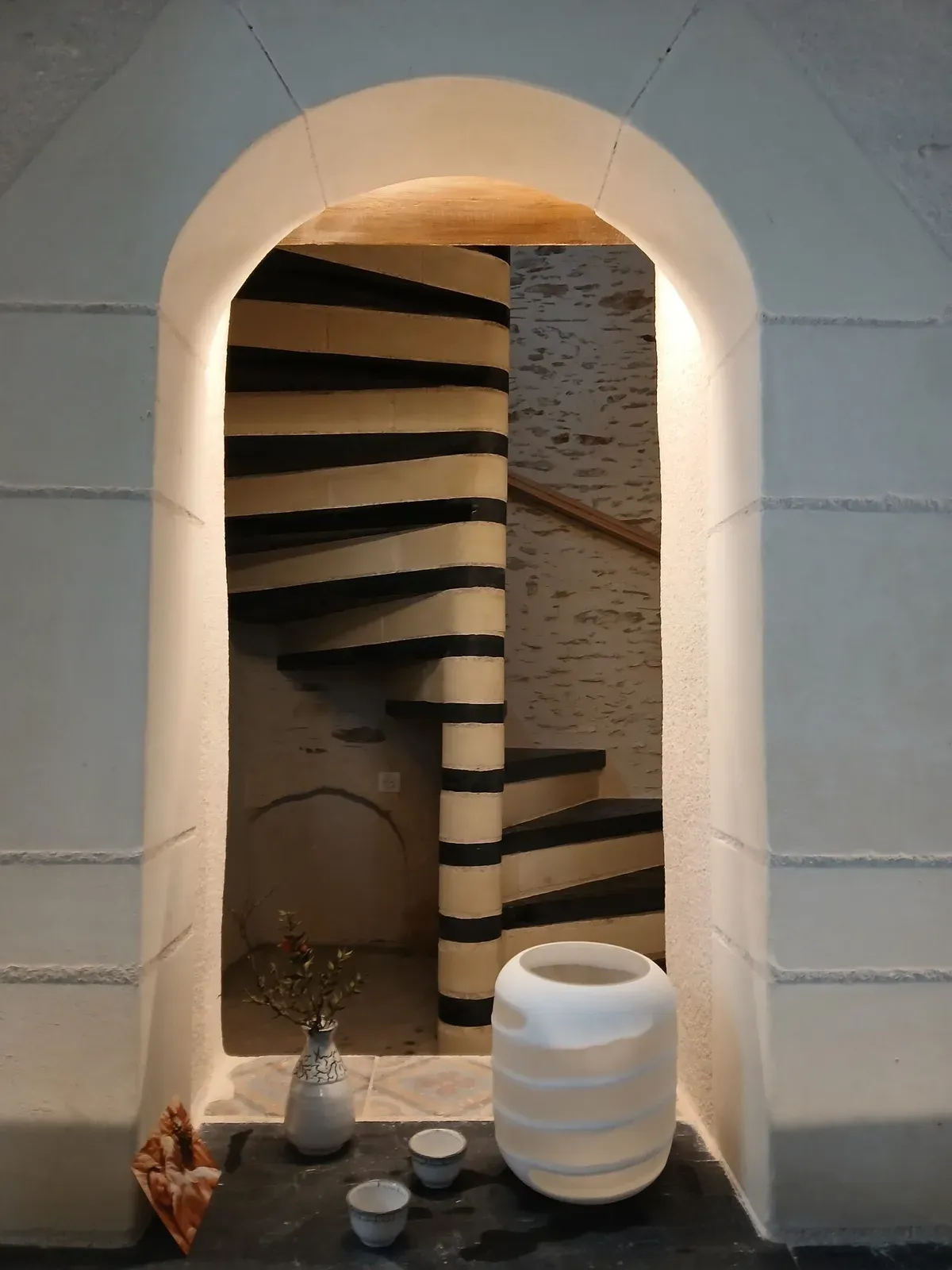 Escalier à noyau en pierre vu à travers une arche en tuffeau